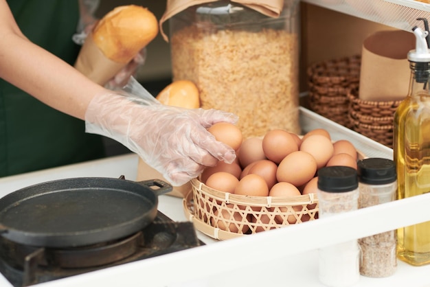 Hands in desposable gloves taking fresh chicken eggs out of basket to make dish