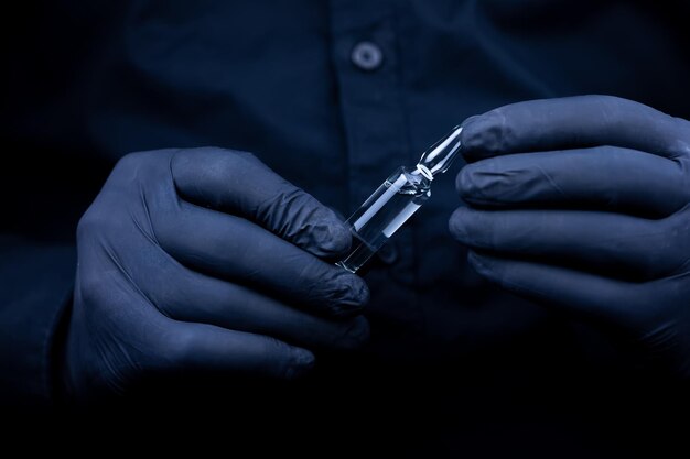 The hands of a doctor in black medical gloves who turns over an ampoule with a vaccine