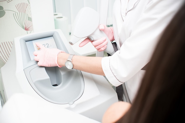 Le mani del medico in guanti rosa tengono il dispositivo per un'epilazione e premono il touch screen. il concetto di dispositivo di controllo, epilazione laser