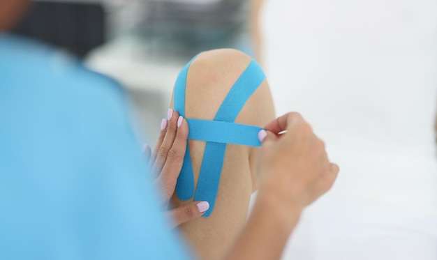 Hands of doctor sticking tape on knee of athlete closeup