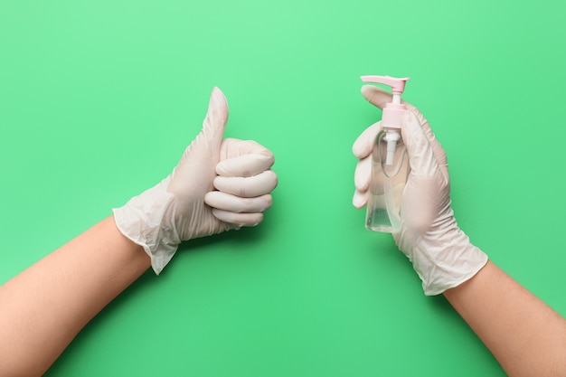 Hands of doctor with disinfectant showing thumb-up gesture on color surface