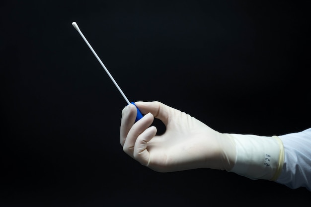 Hands of doctor with sterile gloves holding PCR test sample for Covid-19 in profile, black background