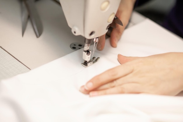 Hands of a dressmaker sewing clothes from white fabric on a sewing machine closeup