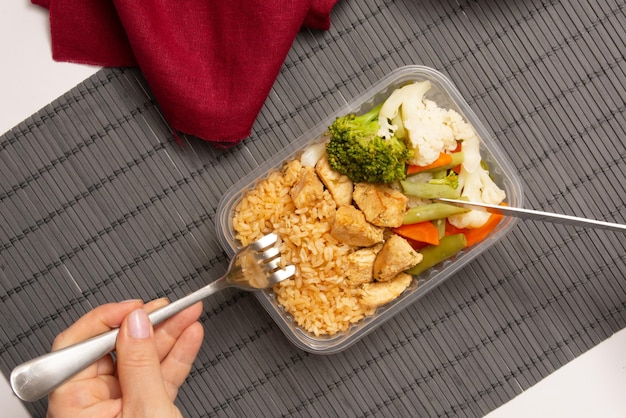 Hands eating packed lunch box home prepared meal in aerial top view wood background