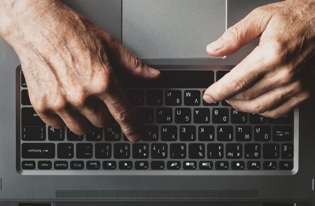 Hands of an elderly man learning to use computer, typing on a laptop, view from above