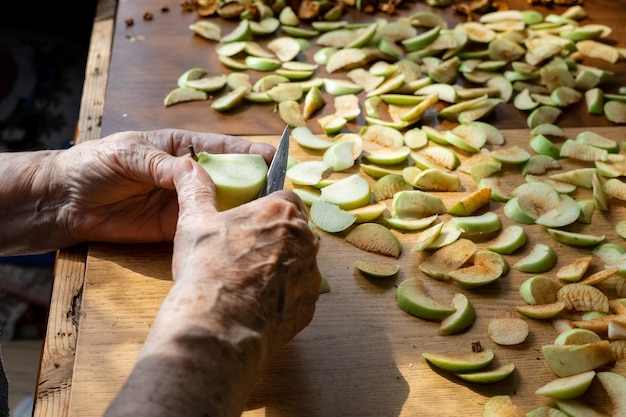 Photo the hands of an elderly woman cut an apple into slices for harvesting