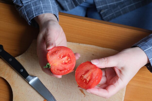 Hands of an elderly woman cutting a red ripe tomato on a cutting board for a snack in the kitchen at a brown table no face closeup