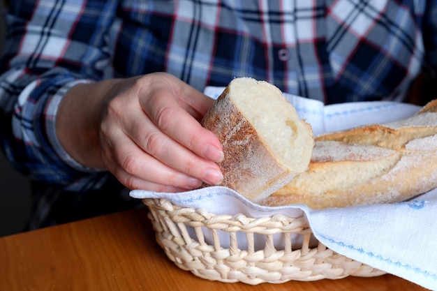 Hands of an elderly woman holding sliced white wheat bread baguette in the kitchen at a brown table no face closeup