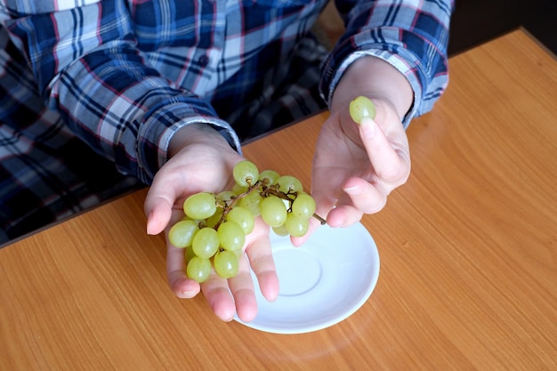 The hands of an elderly woman holds a small brush of white seedless grapes and displays them in the kitchen at a brown table without a face closeup