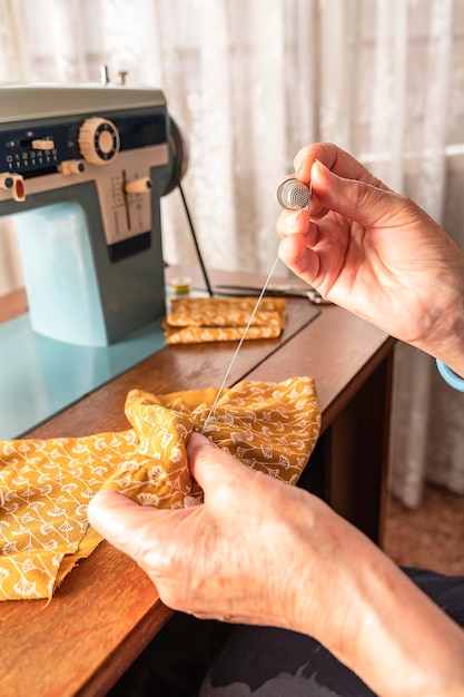 Hands of elderly woman sewing by hand a scrap of orange fabric