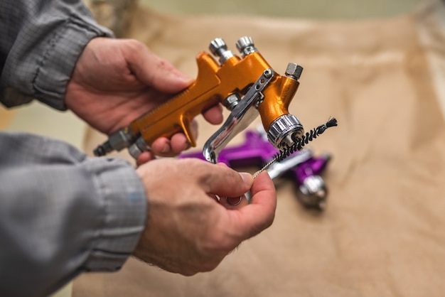 The hands of an employee of the shop painting and cleaning of the spray gun