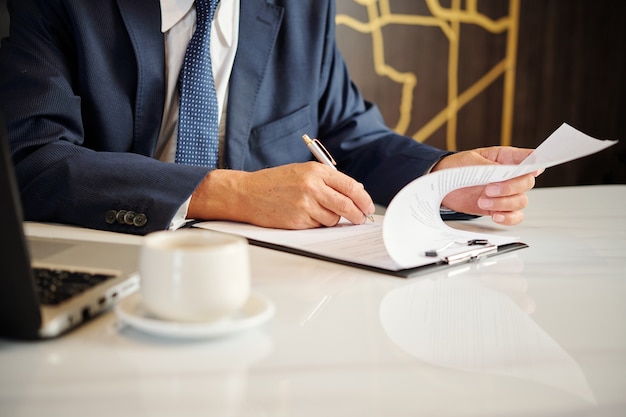 Hands of entrepreneur signing documents and contracts when having morning coffee