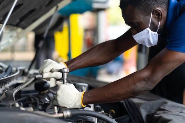 Mani esperto meccanico di automobili nel servizio di riparazione auto. manutenzione auto e concetto di garage servizio auto. uomo di colore che indossa la maschera medica protec virus corona