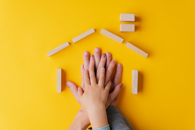 Hands of a father, mother and child one on top of the other placed in a house shape made of wooden pegs