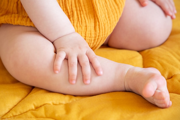 Hands and feet of a child in yellow clothes on a yellow\
blanket