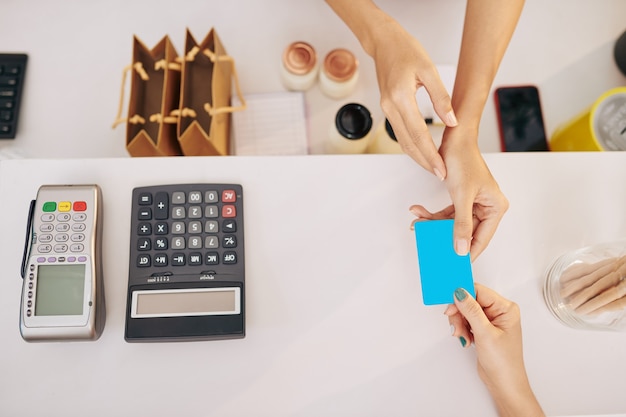 Mani del cliente femminile che dà la carta di credito al barista per pagare l'ordine, vista dall'alto