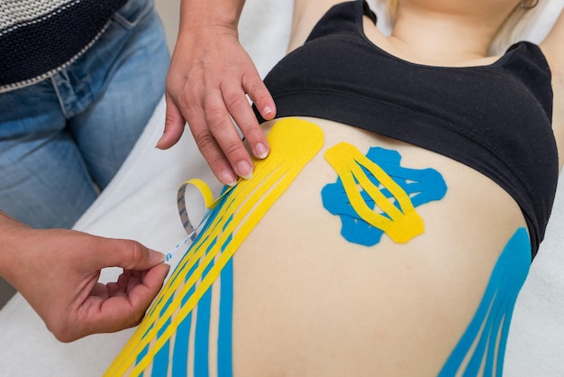 The hands of a female physiotherapist apply adhesive elastic therapeutic tape to the female