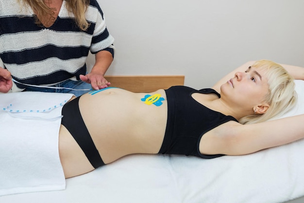 The hands of a female physiotherapist apply adhesive elastic therapeutic tape to the female