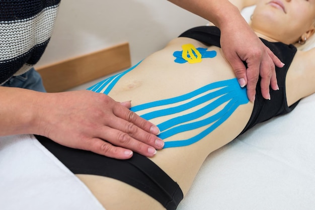 The hands of a female physiotherapist apply adhesive elastic therapeutic tape