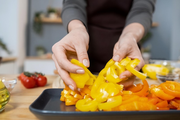 Hands of female putting chopped fresh yellow capsicum on tray