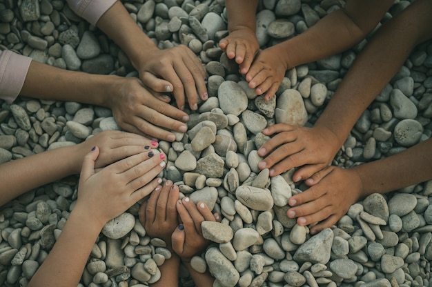 Hands of five children making a circle over pebbles.