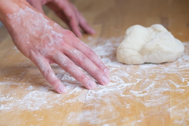 Hands in flour next to lump of dough on wooden board, person kneading dough