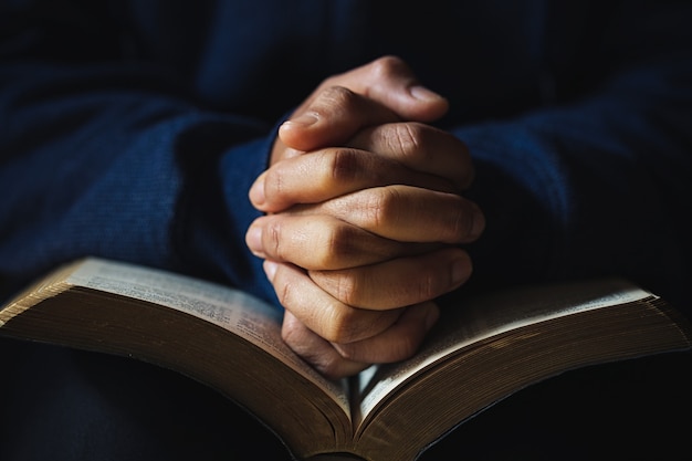 Руки сложены в молитве на Святой Библии в церкви концепции для веры