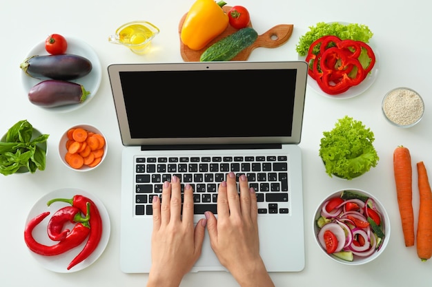 Foto mani di food blogger con laptop e prodotti diversi sul tavolo bianco