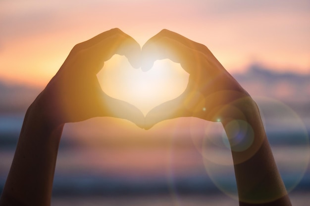 Hands forming a heart shape with sunset silhouette