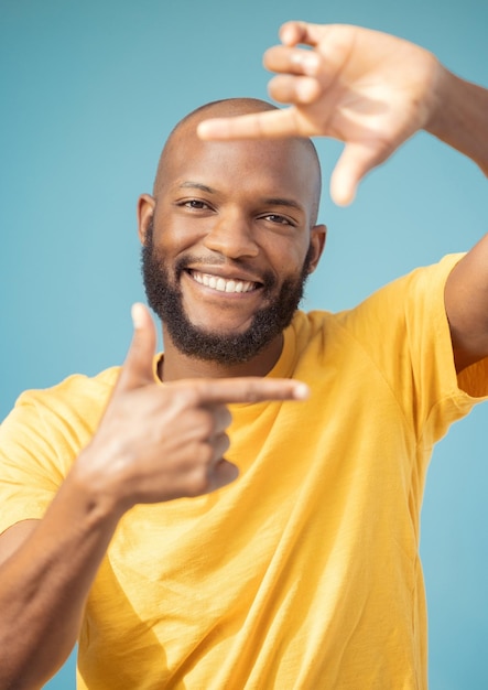Photo hands frame and portrait of black man on blue background for profile picture face happy guy and finger framing for perspective selfie and vision of happiness smile and photography sign in studio