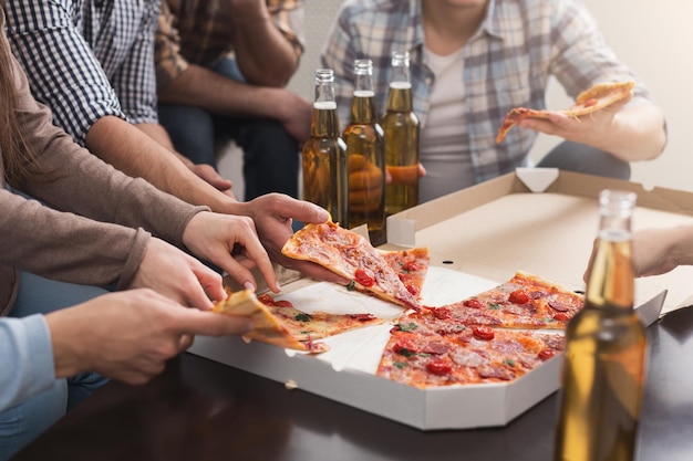 골판지 상자에서 맛있는 피자 조각을 가져오고 집에서 병으로 마시는 친구들의 손. 우정, 여가, 휴식, 홈 파티 개념