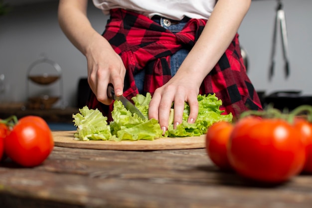 少女の手がテーブルの上でレタスを切り、女性が野菜サラダを準備し、健康食品をナイフで切り刻みます