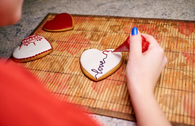 Hands of a girl paint homemade heart-shaped cookies with patterns