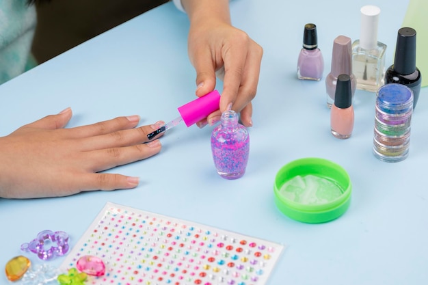 Hands of a girl painting her nails with varnish on a blue table