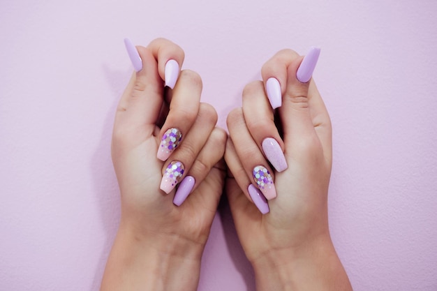 Foto le mani della ragazza mostrano una manicure professionale con smalto per unghie su sfondo viola