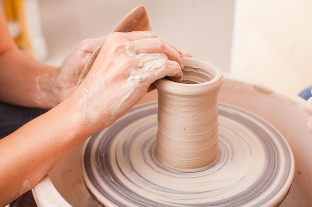 Hands of girl who makes pottery from white clay on a potters wheel