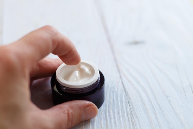 Hands of a girl with a jar of face cream close up applied to the finger of woman's hand