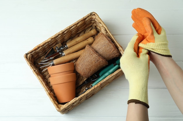 Hands in gloves and basket with gardening tools, top view