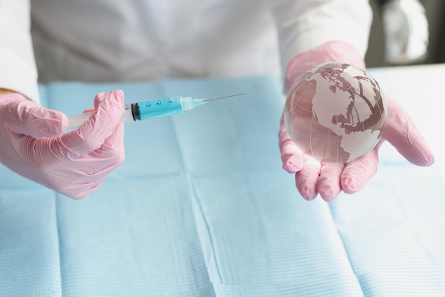 Hands in gloves direct the syringe to a glass transparent globe, close-up. Booster vaccination, global health, pandemic