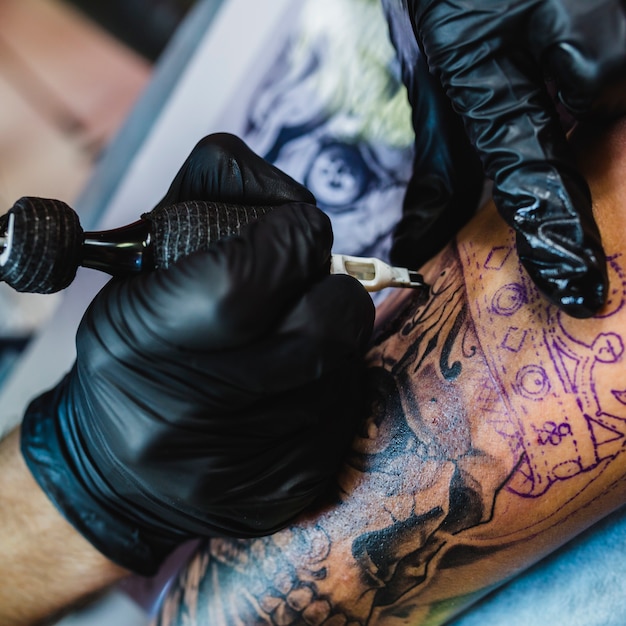 Photo hands in gloves drawing tattoo with tool