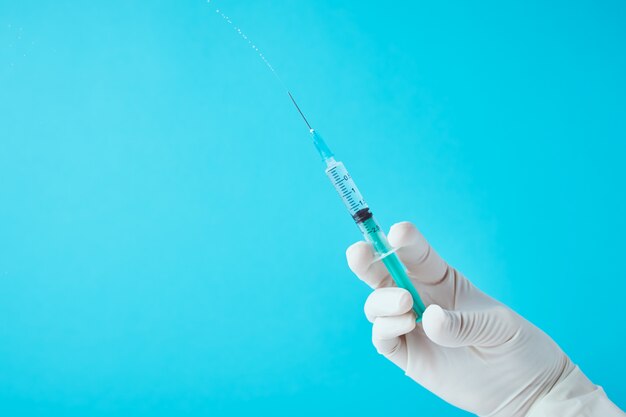 Hands in gloves hold injection syringe against blue background.  Healthcare, medical and virus protection concept