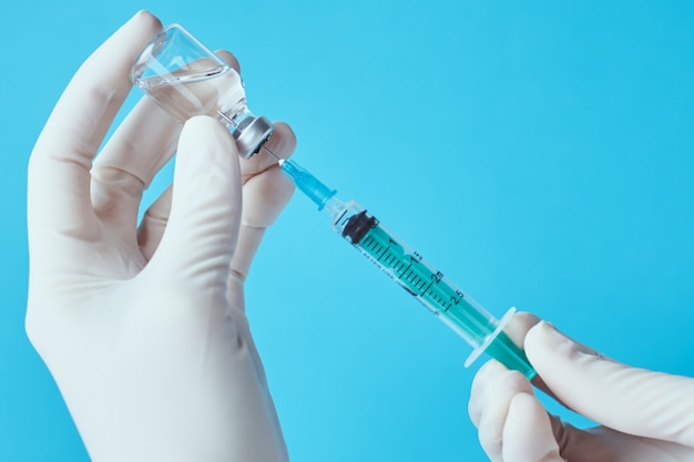 Hands in gloves hold injection syringe against blue background.