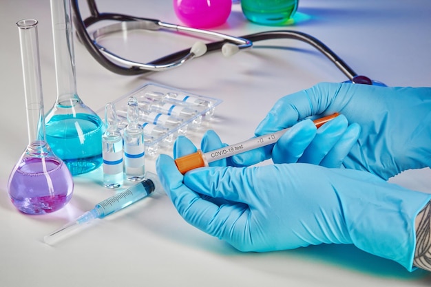 Hands in gloves holding coronavirus testing kit medical flasks with colorful chemical reagents ampou