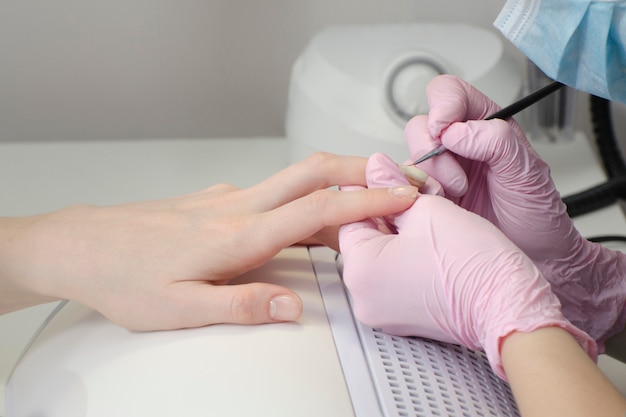 Hands in gloves paint nails in the salon of a manicure. Close up