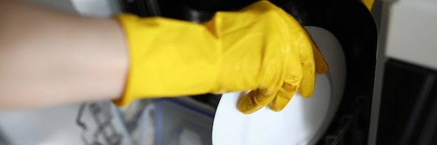 Hands in gloves put plate to dishes in dishwasher