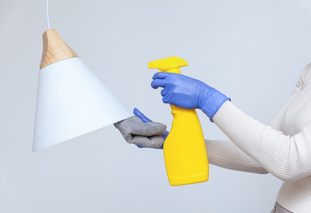 Hands in gloves removing dust cleaning electric lamp chandelier