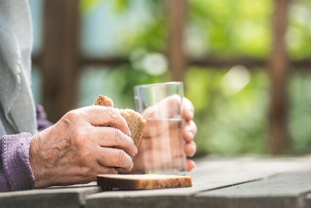 Hands of the grandmother hold a glass and bread on a wooden table