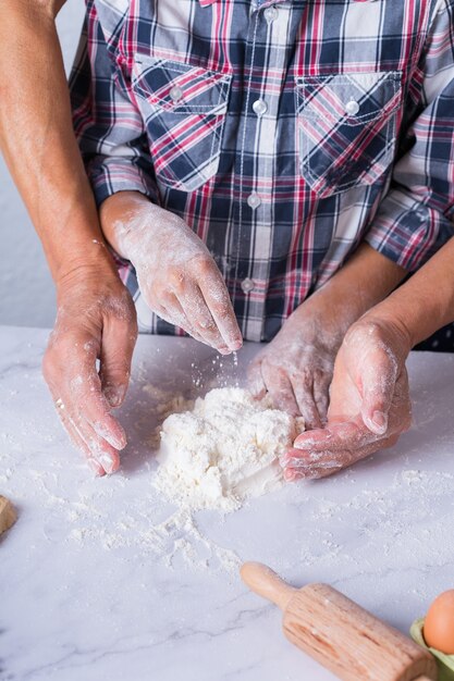 Hands of grandmother and young boy, grandson cooking, kneading dough, baking pie, cake, cookies. Family time in the cozy kitchen. Activity at home.