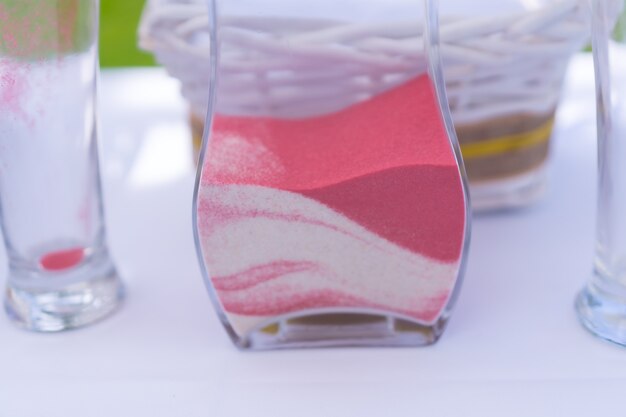 Hands of the groom and bride performing the sand ceremony in a glass vase at the wedding celebration