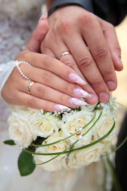 Hands of the groom and the bride with wedding rings hold a wedding bouquet from white roses close up